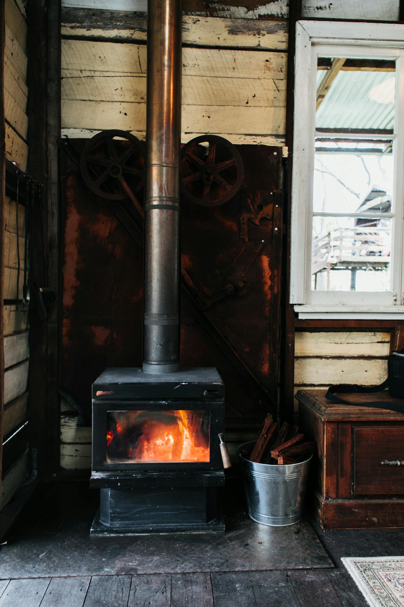 Interior of vintage styled room with fireplace with burning firewood and metal pipe placed near wooden walls and bucket near window