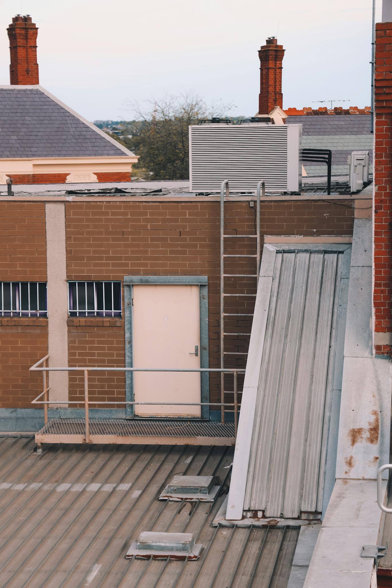 View of an urban rooftop with brick buildings, HVAC unit and ladder.